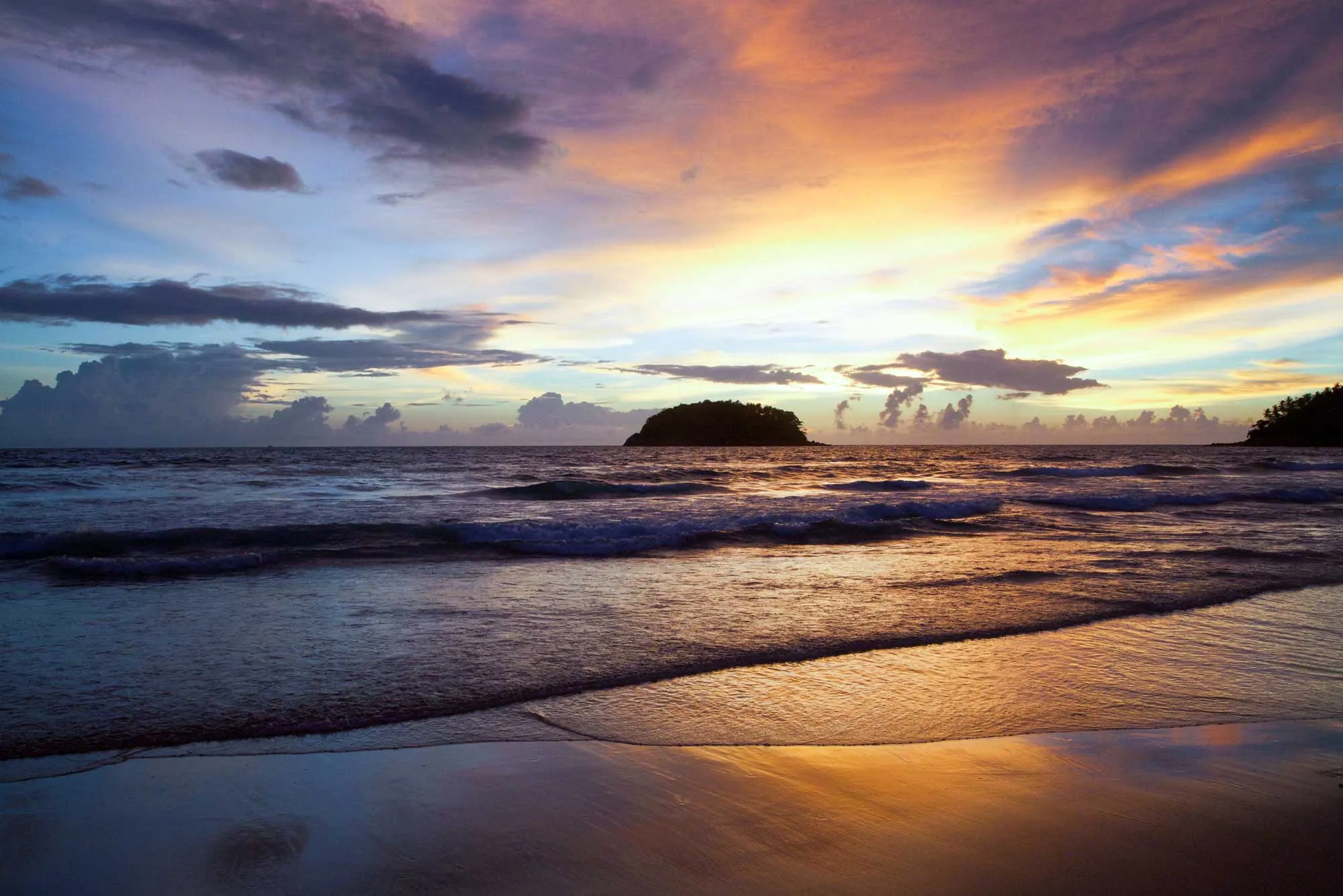 A vibrant sunset paints the sky in hues of orange and pink over the calm ocean and sandy beach.